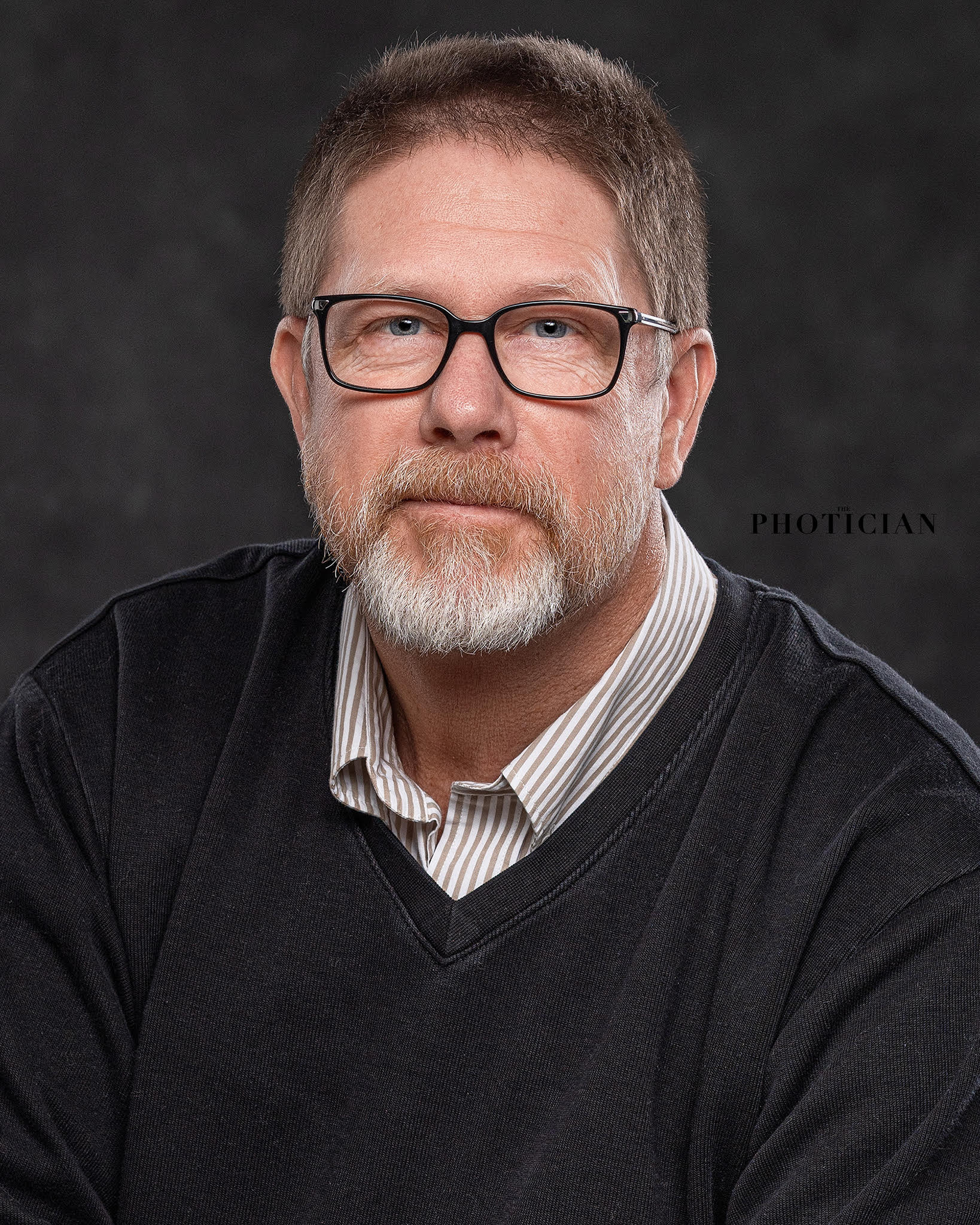 Sean Whalen seated against a dark studio backdrop, wearing glasses and a dark sweater.
